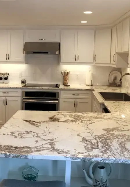 A kitchen with white cabinets and marble counter tops.